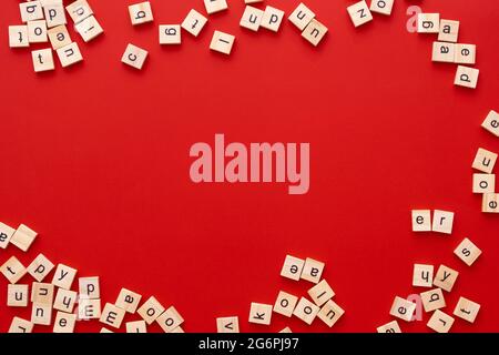 Immagine di sfondo le lettere sono sparse in disordine. Lettere inglesi. Lettere quadrate di legno su sfondo rosso brillante. Biglietto d'auguri, pronto all'uso Foto Stock