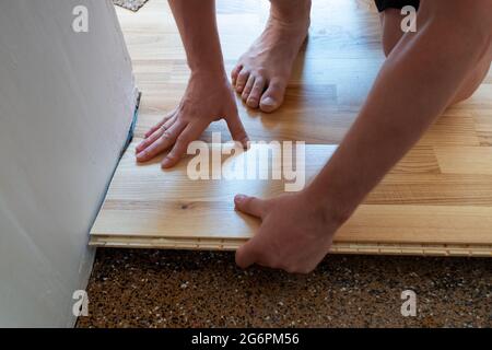Uomo caucasico che installa pannelli di parquet in legno durante i lavori di pavimentazione Foto Stock