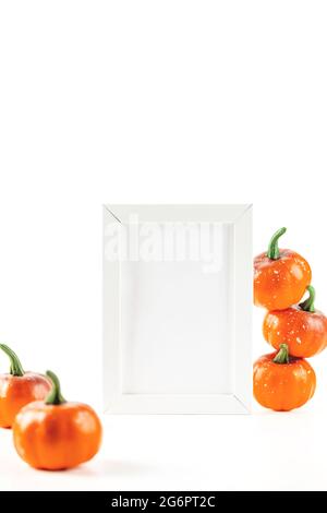 Mockup per carta d'invito autunno o design in cornice bianca accanto alle zucche arancioni su sfondo bianco. Foto Stock