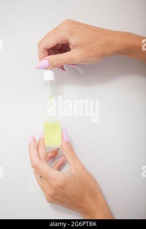 Shot verticale tagliato di mani femminili che tengono in mano il flacone di olio per cuticola con pipetta Foto Stock