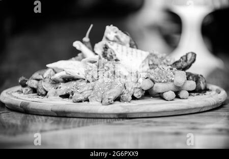 Tavola di legno con patatine fritte molto bastoni di pesce burrito e bistecca di carne servita con insalata. Menu pub snack. Spuntino ad alta caloria per amici di gruppo. Gustoso Foto Stock