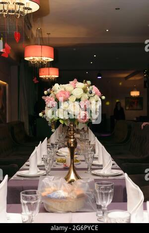 Tavolo splendidamente servito in un ristorante con un bouquet di fiori bianchi e rosa in un vaso d'oro Foto Stock