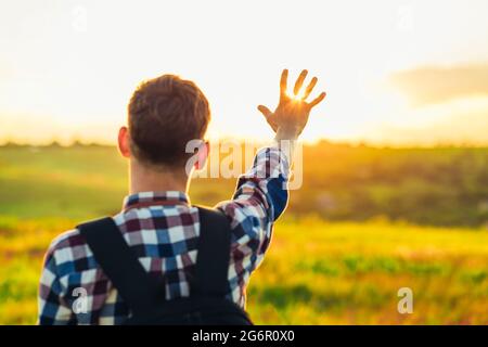 Vista posteriore, mano umana, turista che copre la luce del sole, sole che splende attraverso la mano, mano umana e sole, concetto di viaggio, turismo Foto Stock