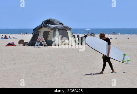 Los Angeles, Stati Uniti. 8 luglio 2021. Un surfista cammina attraverso una tenda senza dimora a Venice Beach a Los Angeles mercoledì 7 luglio 2021. Fliers inviato dalla città ha delineato una cinque settimane 'ripresa graduale delle normali operazioni' con una 'pulizia completa fronte mare' della zona, che è sotto la giurisdizione della città Recreation and Parks Department. L'avvertimento ha detto 'ai residenti non ospitati che attualmente vivono nel parco sarà offerto alloggio.' Foto di Jim Ruymen/UPI Credit: UPI/Alamy Live News Foto Stock