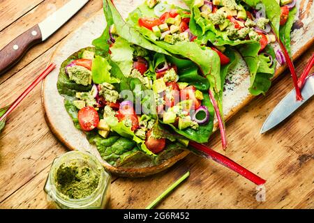 Insalata di avocado, pomodoro con salsa al pesto in foglie di bietole. Insalata di vitamina estiva su tavola da cucina Foto Stock