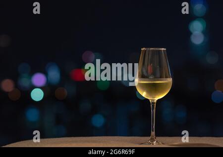 Un bicchiere di vino bianco mette sul divano la colorata luce bokeh della città. Foto Stock