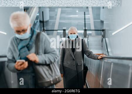 i passeggeri che indossano maschere protettive mantengono la distanza mentre si trovano sulla scala mobile della metropolitana. regole della città durante la pandemia. Foto Stock