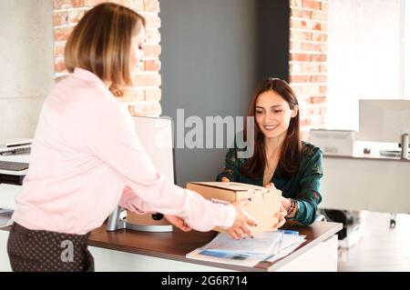 Allegro manager donna sorridente e prendendo scatola di cartone da donna consegna mentre lavora in ufficio Foto Stock