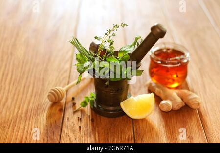 Mazzetto di erbe fresche e pestello posto in mortaio di ottone vicino alla radice di zenzero e limone per una sana preparazione del tè sul tavolo Foto Stock