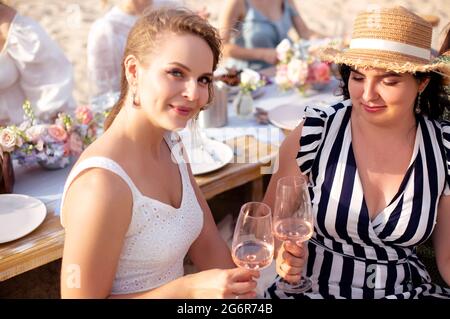 Felici le donne che sorridono e graffiano i bicchieri di vino mentre propongono il toast durante il banchetto il giorno d'estate Foto Stock