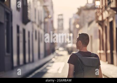 Vista posteriore del viaggiatore singolo. Giovane uomo con zaino sulla strada della città vecchia. San Cristóbal de la Laguna a Tenerife, Isole Canarie, Spagna. Foto Stock