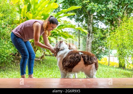 giovane donna che accarezzava i suoi due cani nel giardino della sua casa Foto Stock