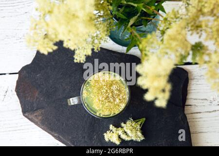 Moderna vista dall'alto attraverso il fresco fiore di MeadowSweet, Filipendula ulmaria in vaso per la stessa pianta tisana in vetro. Foto Stock