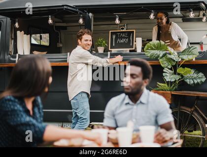 Persone multirazziali che mangiano al camion del cibo all'aperto - Focus sulla faccia dell'uomo centrale Foto Stock