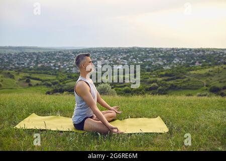 Yoga. Un uomo con capelli grigi pratica la meditazione sulla natura in estate. Foto Stock