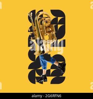 Arte moderna, design e musica. Grande tuba dorata sulle gambe maschili in stivali eleganti su sfondo giallo con motivo geometrico. Foto Stock