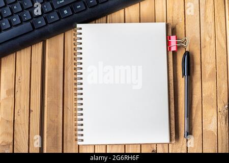 Vuota il giornale tagliato accanto A UNA Keyboard Pen sulla parte superiore della scrivania in legno. Blocco note vuoto aperto con clip e matita vicino alla tastiera posizionati sul tavolo. Foto Stock