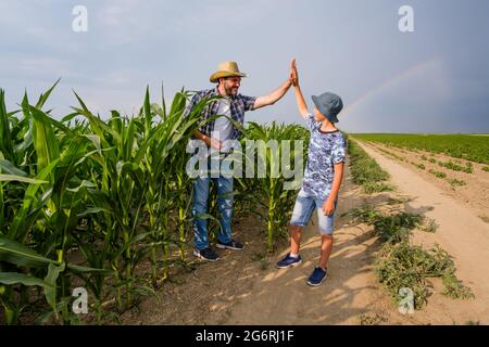 Padre sta insegnando a suo figlio a coltivare il mais. Piantagione di mais seminata con successo. Agricoltori in campo agricolo. Foto Stock