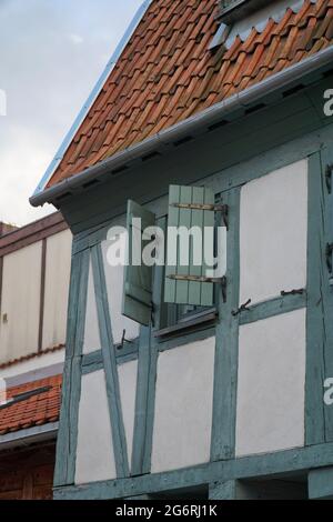 Particolare di una parete di casa a graticcio con finestra, ferramenta e persiane a mezza apertura in bianco, verde e grigio. Tegole rosse sul tetto. Klaipeda, L. Foto Stock