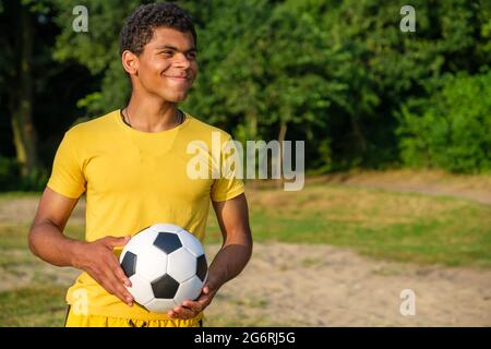 Felice uomo afroamericano che tiene la palla di calcio mentre si trova all'aperto nel parco Foto Stock