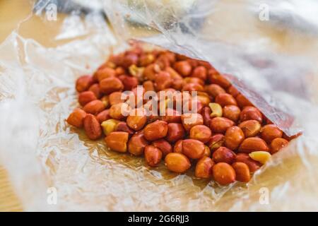 Mangia le arachidi salate in guscio rosso dal sacchetto di plastica su sfondo bianco sull'isola di Koh Samui in Thailandia. Foto Stock