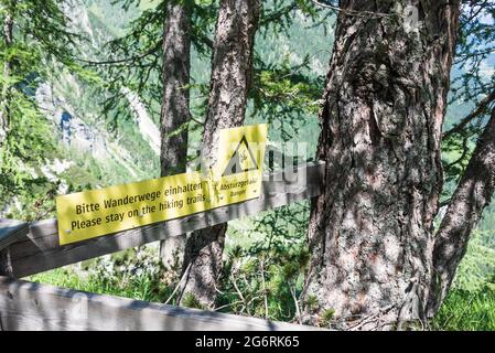Il cartello giallo con lettere nere in tedesco e inglese sul sentiero dicendo. Bitte Wanderwege einhalten, absturzgefahr, si prega di rimanere sul Foto Stock