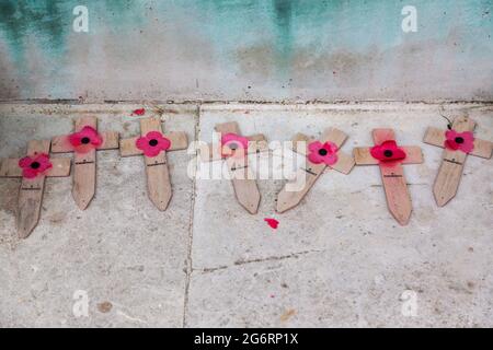 Legno intemperie attraversato da papaveri rossi sbiaditi deposti in un memoriale di guerra Foto Stock