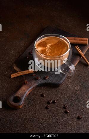 Caffè caldo e aromatico che si spillano dalla tazza di vetro sullo sfondo scuro Foto Stock