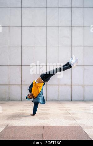 Ballerino cool che fa la mano in strada contro la parete bianca e guardando la macchina fotografica. Foto Stock