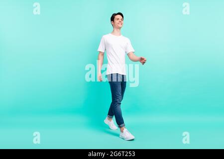 Foto profilo a lunghezza intera di divertente brunet hairdo teenager guy go look spazio vuoto indossare t-shirt jeans isolato su sfondo teal Foto Stock