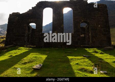 Silhouette della cappella o chiesa di Rhosydd gallese in rovina, retroilluminata dal sole, archi e ombre che illuminano il terreno. Moody Gothic, paesaggio. Cwmortin, Bl Foto Stock