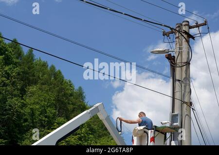 Uomo che installa una telecamera di sicurezza su un pilone elettrico per monitorare i luoghi pubblici in un villaggio in Slovacchia. L'uomo è in piedi su una piattaforma idraulica. Foto Stock