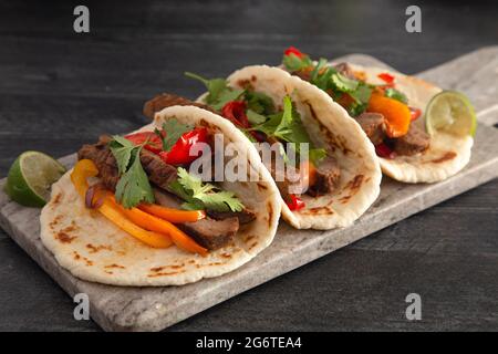 Fajitas di manzo con peperoni su un tavolo di legno scuro Foto Stock