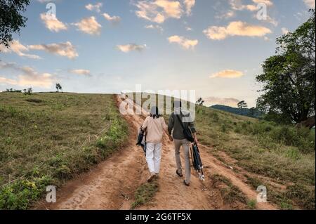 Retro di giovane coppia asiatica sedia da trasporto e stoffa che cammina su verde collina in campagna alla sera Foto Stock