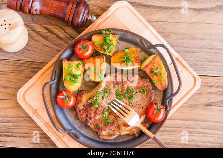 Bistecche di maiale arrosto in padella di carne al collo con patate. Sfondo in legno Foto Stock