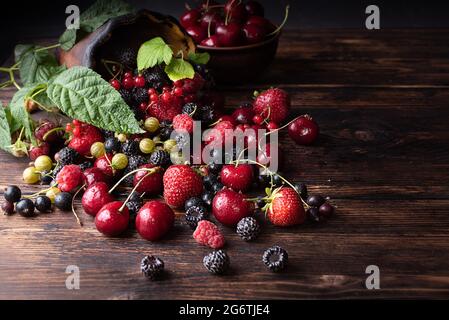 Frutti di bosco estivi, lamponi, fragole, ciliegie, ribes sparsi su un tavolo di legno scuro, cibo sano, primo piano. Foto Stock