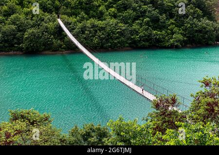 Ragazzo che guarda giù il ponte sospeso o sospeso sul bel fiume smeraldo, Albania Foto Stock