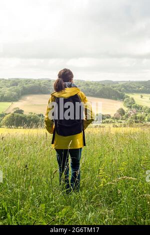 Donna camminatore con giacca gialla e uno zaino godendo la vista sulla campagna sopra le Downs Sussex. Foto Stock