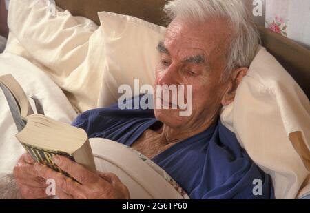 uomo anziano a letto che legge un libro Foto Stock