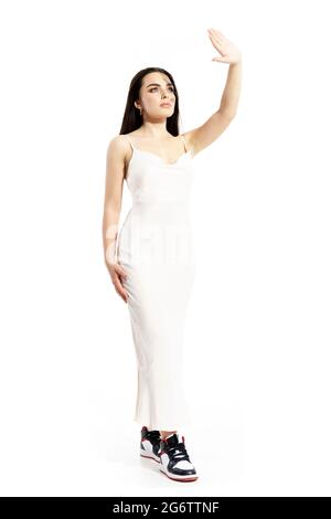 Vogue giovane bella donna in bianco elegante abito che protegge la luce solare dagli occhi. Ritratto a corpo intero isolato su sfondo bianco Foto Stock