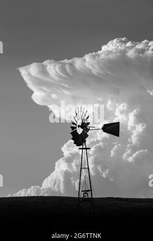 Un enorme thunderhead cresce all'orizzonte dietro un mulino a vento sulla prateria del Wyoming Foto Stock