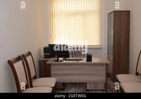 Business Office con un tavolo di legno sul quale si trova un computer, stampante, cancelleria, con una grande finestra sul retro, sedie e un armadio Foto Stock