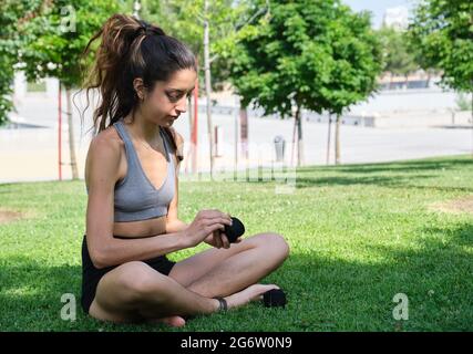 Nessuna persona binaria che indossa le mani muay thai avvolge seduti sull'erba in un parco. Sport all'aperto. Foto Stock