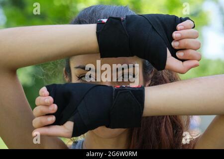 Nessuna persona binaria in mano si avvolge in posa con le mani dietro il viso. Sport all'aperto. Foto Stock