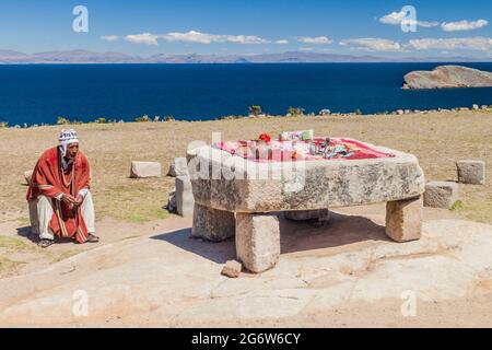 ISLA DEL Sol, BOLIVIA - 12 MAGGIO 2015: L'uomo nativo in abiti tradizionali accanto alla tavola Ceremonial usato per essere probabilmente luogo di sacrifici umani a. Foto Stock