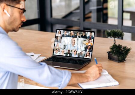 Dirigente maschile caucasico, avendo online meeting virtuale tramite videoconferenza con colleghi multirazziali di successo, utilizzando il laptop, seduto in ufficio, pianificazione strategia di marketing e idee Foto Stock