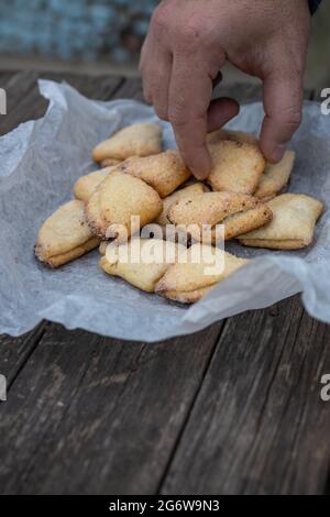 La mano dell'uomo prende i biscotti di shortbread del caglid con i triangoli su pergamena bianca su un vecchio sfondo di legno scuro. Foto Stock