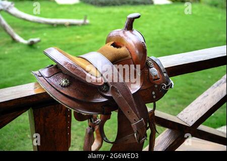 Bella sella cavallo in pelle su una recinzione di legno. Nessun cavallo, erba verde sullo sfondo. Foto Stock