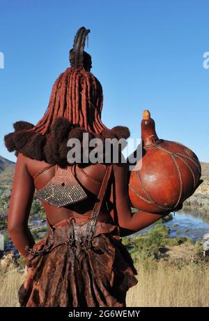 NAMIBIA. GIOVANI DONNE HIMBAS IN CERCA DI ACQUA VICINO ALLE CASCATE EPUPA DEL FIUME KUNENE, CONFINE NATURALE CON L'ANGOLA. QUASI 8 000 HIMBAS VIVONO Foto Stock