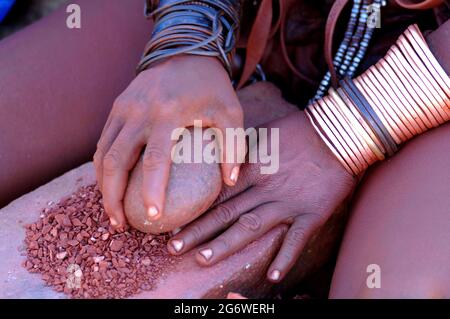 NAMIBIA. HIMBA DONNA CHE PREPARA IL ROSSO TRADIZIONALE OIGNMENT (OTJIRE) CHE USA PER PROTEGGERE LA SUA PELLE DAL SOLE, L'ARIA SECCA E GLI INSETTI. QUESTO OIG Foto Stock
